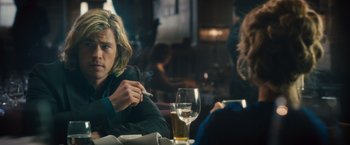 Movie still from “Rush” (2013), directed by Ron Howard – A man sitting at a table smoking a cigarette and drinking a beer; Medium shot, Over the shoulder angle