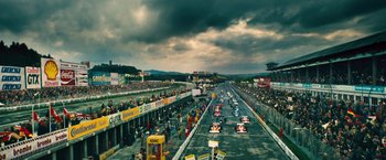 Movie still from “Rush” (2013), directed by Ron Howard – A group of cars driving down a race track under a cloudy sky; Extreme Wide shot, High angle