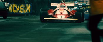 Movie still from “Rush” (2013), directed by Ron Howard – A red and white race car driving down a street; Wide shot, Low angle