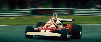 Movie still from “Rush” (2013), directed by Ron Howard – A red and white race car driving down a race track; Wide shot, Low angle