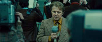 Movie still from “Rush” (2013), directed by Ron Howard – A man holding a microphone in his hand; Medium shot, Over the shoulder angle