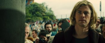 Movie still from “Rush” (2013), directed by Ron Howard – A group of people standing in front of a large crowd; Close Up shot, Over the shoulder angle