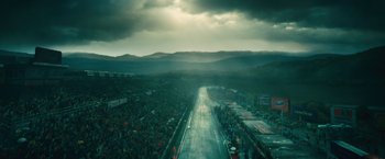 Movie still from “Rush” (2013), directed by Ron Howard – A crowd of people standing on a race track under a cloudy sky; Extreme Wide shot, Low angle
