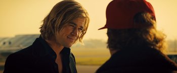 Movie still from “Rush” (2013), directed by Ron Howard – A man with long blonde hair talking to another man wearing a red hat; Close Up shot, Over the shoulder angle