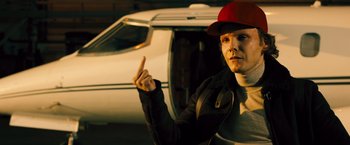 Movie still from “Rush” (2013), directed by Ron Howard – A man wearing a red hat standing in front of an airplane; Medium shot, Over the shoulder angle