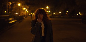 Movie still from “Russian Doll” (2019), created by Natasha Lyonne – A woman standing on a sidewalk at night smoking a cigarette; Medium shot, High angle