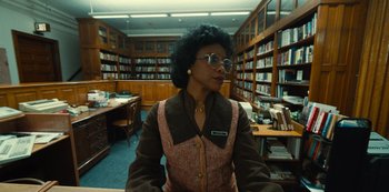 Movie still from “Russian Doll” (2019), created by Natasha Lyonne – A woman sitting at a table in a library; Medium shot, Low angle