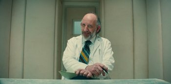 Movie still from “Russian Doll” (2019), created by Natasha Lyonne – An older man wearing a white lab coat and a tie; Close Up shot, Low angle