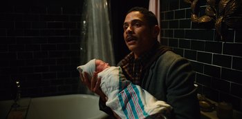 Movie still from “Russian Doll” (2019), created by Natasha Lyonne – A man holding a baby in his arms in front of a tub; Close Up shot, High angle
