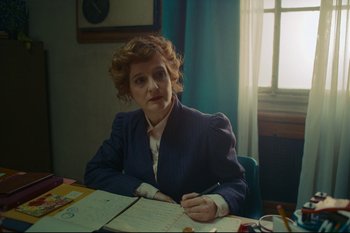 Movie still from “Argentina, 1985” (2022), directed by Santiago Mitre – A woman sitting at a table with a pen and paper; Medium shot, Over the shoulder angle