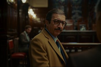 Movie still from “Argentina, 1985” (2022), directed by Santiago Mitre – A man in a suit and tie standing in front of a table; Medium shot, Over the shoulder angle