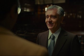 Movie still from “Argentina, 1985” (2022), directed by Santiago Mitre – An older man wearing a suit and tie smiling; Medium shot, Over the shoulder angle