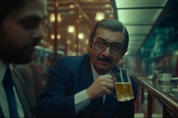 Movie still from “Argentina, 1985” (2022), directed by Santiago Mitre – A man in a suit and tie holding a glass of beer; Close Up shot, Over the shoulder angle