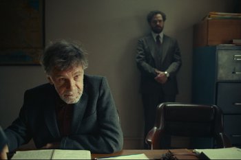 Movie still from “Argentina, 1985” (2022), directed by Santiago Mitre – A man sitting at a desk in front of another man in a suit; Medium shot, Over the shoulder angle