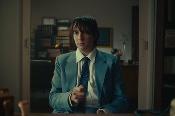 Movie still from “Argentina, 1985” (2022), directed by Santiago Mitre – A man in a suit and tie sitting at a desk; Medium shot, Over the shoulder angle