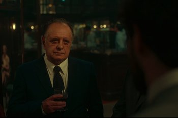 Movie still from “Argentina, 1985” (2022), directed by Santiago Mitre – An older man wearing a suit and tie holding a glass of wine; Medium shot, Over the shoulder angle