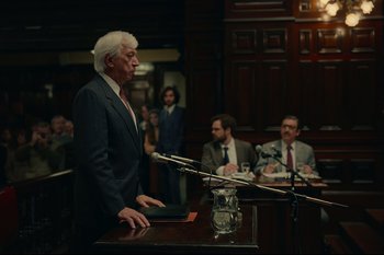 Movie still from “Argentina, 1985” (2022), directed by Santiago Mitre – An older man standing at a podium in front of a group of people; Wide shot, Over the shoulder angle
