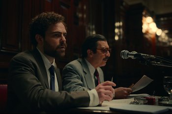 Movie still from “Argentina, 1985” (2022), directed by Santiago Mitre – Two men are sitting at a table and one of them is holding a microphone; Medium shot, Low angle