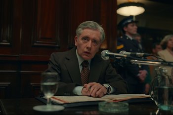 Movie still from “Argentina, 1985” (2022), directed by Santiago Mitre – A man sitting at a table in front of microphones; Medium shot, Over the shoulder angle