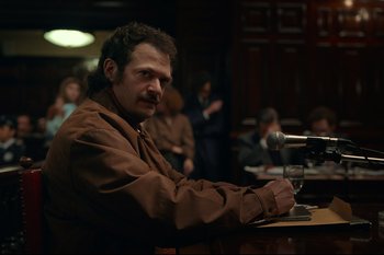 Movie still from “Argentina, 1985” (2022), directed by Santiago Mitre – A man sitting in front of microphones in a courtroom; Medium shot, Over the shoulder angle