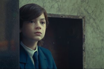 Movie still from “Argentina, 1985” (2022), directed by Santiago Mitre – A boy in a suit and tie looking at the camera; Close Up shot, Low angle
