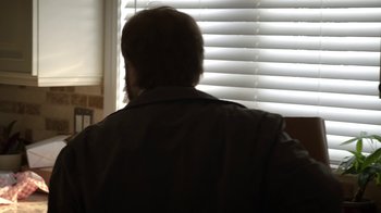 Movie still from “Salvation” (2017), created by Elizabeth Kruger – A man standing in front of a window with blinds open; Medium shot, Over the shoulder angle