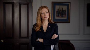Movie still from “Salvation” (2017), created by Elizabeth Kruger – A woman in a suit standing in front of a painting; Medium shot, Low angle