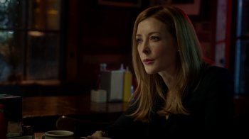 Movie still from “Salvation” (2017), created by Elizabeth Kruger – A woman sitting at a table in a dark room; Close Up shot, Over the shoulder angle