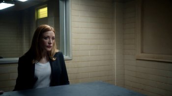 Movie still from “Salvation” (2017), created by Elizabeth Kruger – A woman sitting at a table in front of a brick wall; Medium shot, Over the shoulder angle