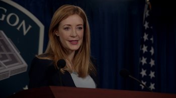 Movie still from “Salvation” (2017), created by Elizabeth Kruger – A woman standing at a podium in front of microphones; Close Up shot, Over the shoulder angle