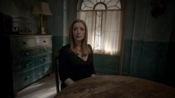 Movie still from “Salvation” (2017), created by Elizabeth Kruger – A woman sitting at a table in front of a window; Medium shot, Over the shoulder angle