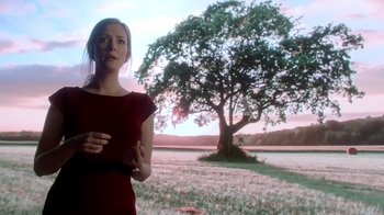 Movie still from “Salvation” (2017), created by Elizabeth Kruger – A woman standing in front of a tree in a field; Medium shot, Low angle