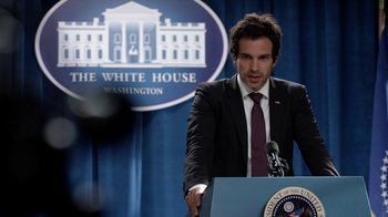Movie still from “Salvation” (2017), created by Elizabeth Kruger – A man standing at a podium in front of the white house; Close Up shot, Over the shoulder angle