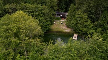 Movie still from “Salvation” (2017), created by Elizabeth Kruger – A group of people sitting around a pond in the middle of a forest; Extreme Wide shot, High angle