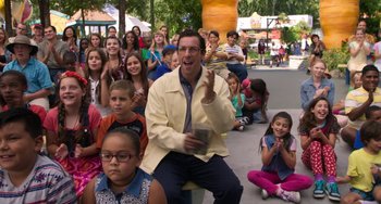 Movie still from “Sandy Wexler” (2017), directed by Steven Brill – A group of people sitting in a circle with a man holding a cell phone; Medium shot, Over the shoulder angle