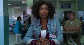 Movie still from “Sandy Wexler” (2017), directed by Steven Brill – A woman sitting at a table with her hands crossed; Medium shot, Over the shoulder angle