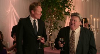 Movie still from “Sandy Wexler” (2017), directed by Steven Brill – Two men in suits are drinking wine at a party; Medium shot, Over the shoulder angle