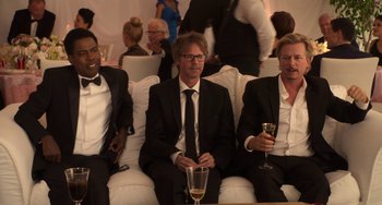 Movie still from “Sandy Wexler” (2017), directed by Steven Brill – A group of men sitting on a white couch with wine glasses; Medium shot, High angle