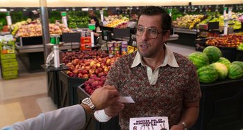 Movie still from “Sandy Wexler” (2017), directed by Steven Brill – A man in a grocery store holding an item in front of him; Medium shot, Over the shoulder angle