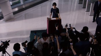Movie still from “Sense8” (2015), directed by Tom Tykwer – A group of people gathered around a podium with microphones in it; Extreme Wide shot, High angle
