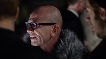 Movie still from “Sense8” (2015), directed by Tom Tykwer – A bald man with glasses and a fur collar; Close Up shot, Over the shoulder angle