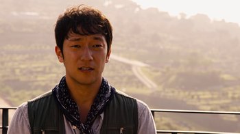 Movie still from “Sense8” (2015), directed by Tom Tykwer – A man with a bandana around his neck is standing in front of a hill; Close Up shot, Over the shoulder angle