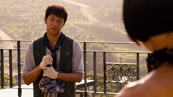 Movie still from “Sense8” (2015), directed by Tom Tykwer – A man holding a purse while standing on top of a building; Medium shot, Over the shoulder angle