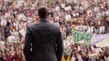 Movie still from “Sense8” (2015), directed by Tom Tykwer – A man in a suit standing in front of a crowd of people; Wide shot, Over the shoulder angle