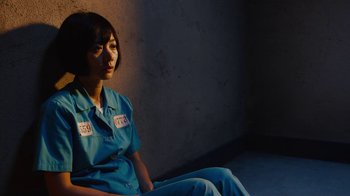 Movie still from “Sense8” (2015), directed by Tom Tykwer – A woman sitting in a dark room wearing a blue shirt; Medium shot, High angle