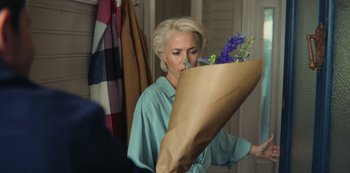 Movie still from “Sex Education” (2019), created by Laurie Nunn – A woman holding a bouquet of flowers in front of her face; Medium shot, Over the shoulder angle