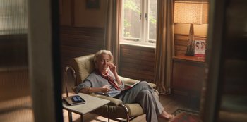 Movie still from “Sex Education” (2019), created by Laurie Nunn – An older woman sitting in a chair in front of a window; Wide shot, High angle