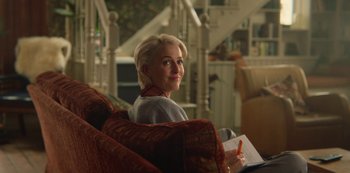 Movie still from “Sex Education” (2019), created by Laurie Nunn – A woman sitting on a couch holding a pen and paper; Medium shot, Over the shoulder angle