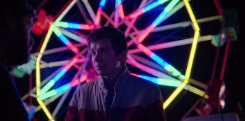 Movie still from “Sex Education” (2019), created by Laurie Nunn – A man standing in front of a ferris wheel at night; Medium shot, Low angle