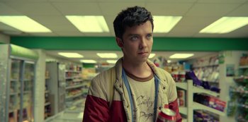 Movie still from “Sex Education” (2019), created by Laurie Nunn – A young man standing in a store holding a cup; Close Up shot, Low angle